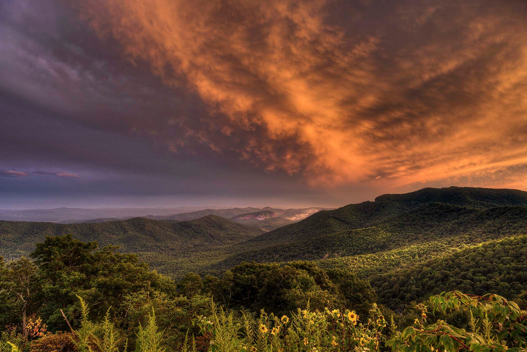 Dramatic orange and purple storm clouds over the forested Blue Ridge mountains at sunset