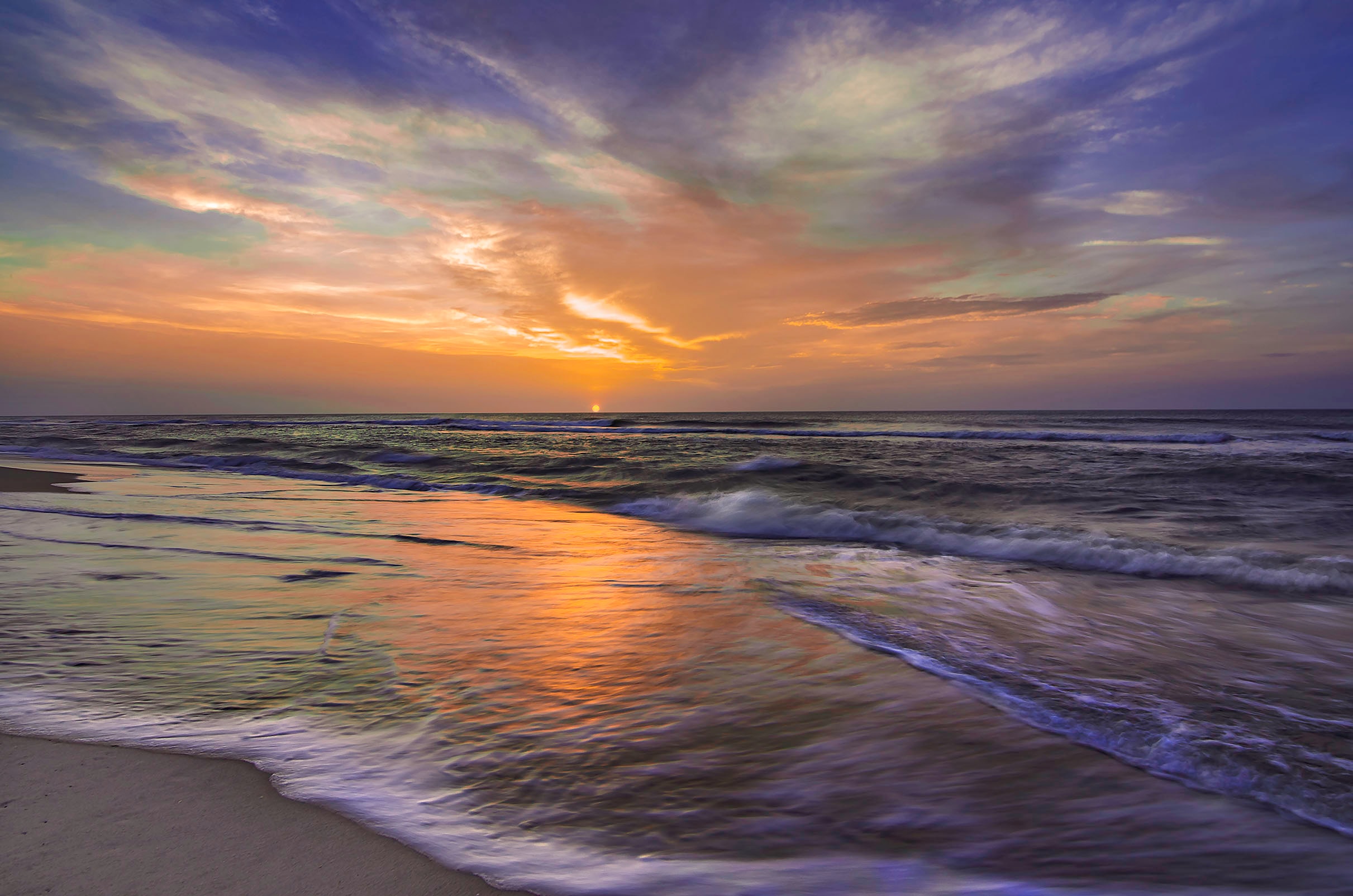 Sunrise over the Atlantic at the Outer Banks, golden light reflected in the wet sand as waves wash ashore