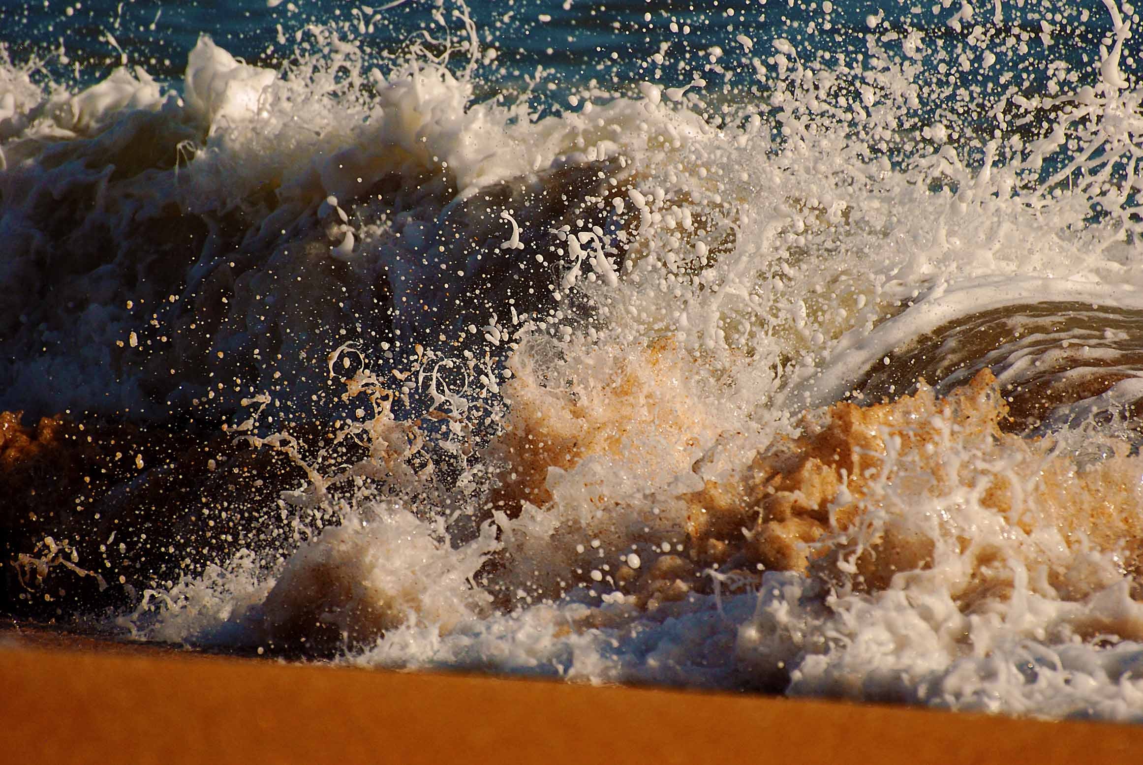 A wave exploding in a burst of white foam and spray in warm golden light