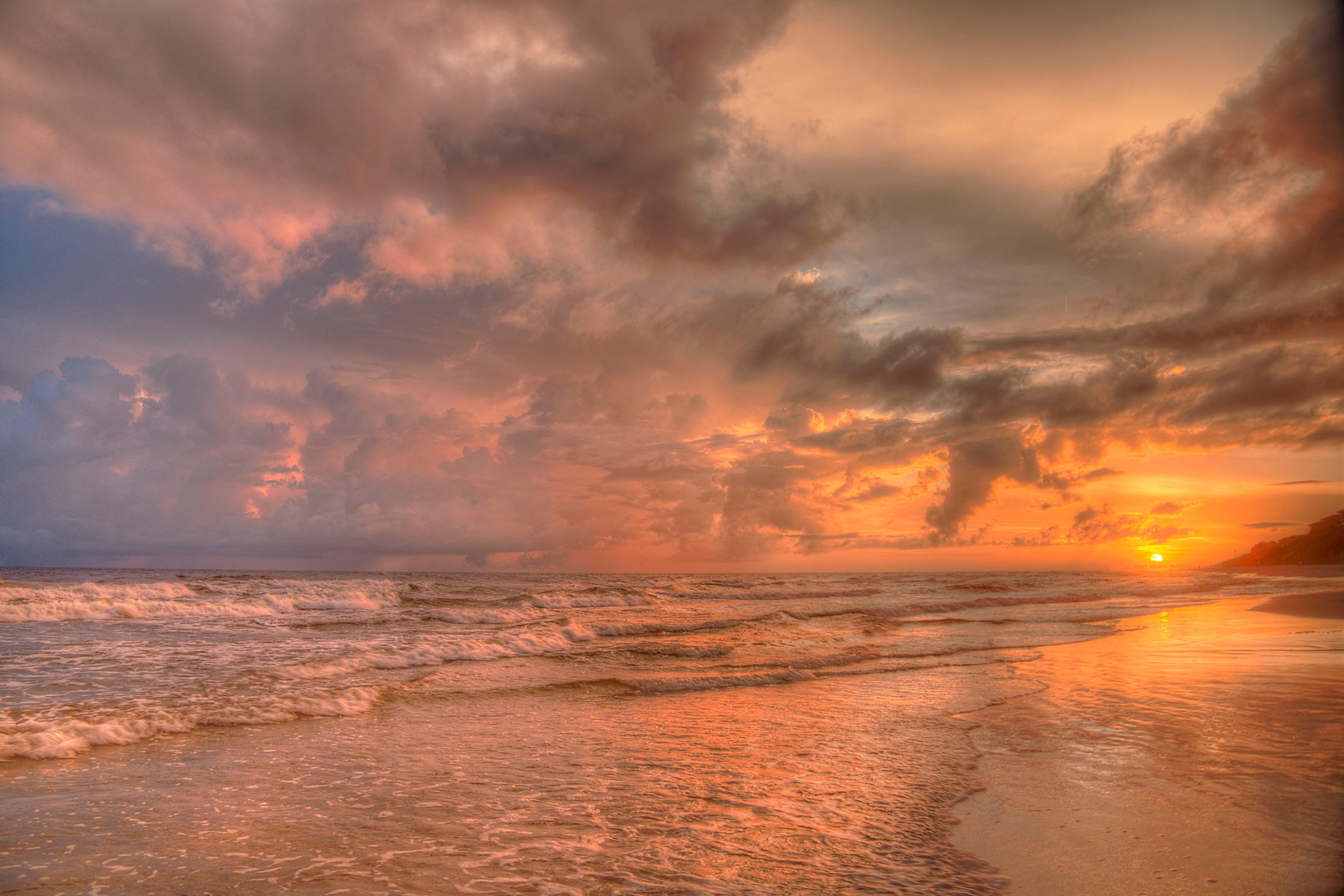 Rolling waves washing ashore at Santa Rosa Beach beneath a blazing orange and copper sunset sky with dramatic storm clouds