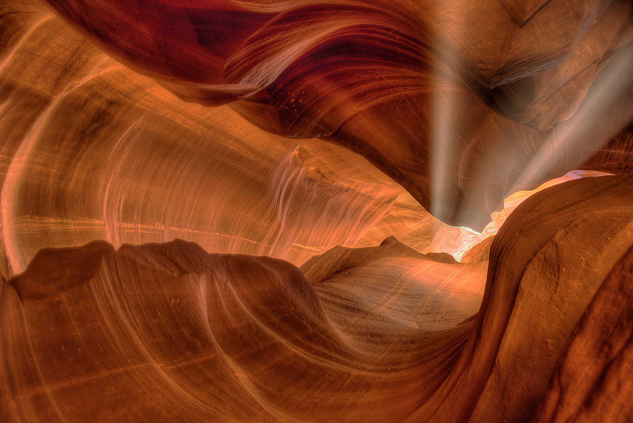 Sunbeams pouring down through the narrow opening of Upper Antelope Canyon, illuminating swirling waves of orange and copper sandstone