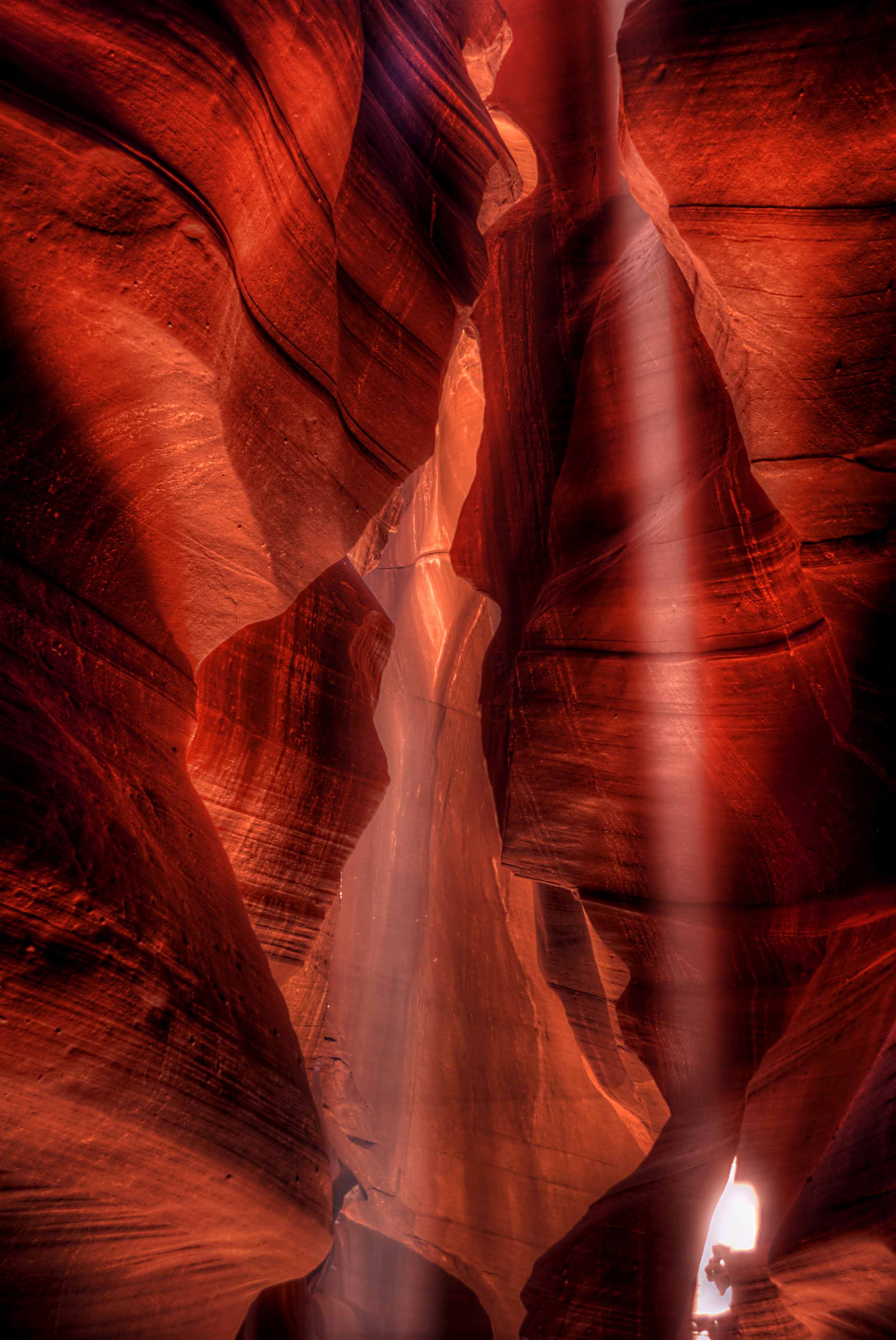 Dramatic sunbeams slicing through the crimson walls of Upper Antelope Canyon, light and shadow sculpting the ancient sandstone into waves of fire