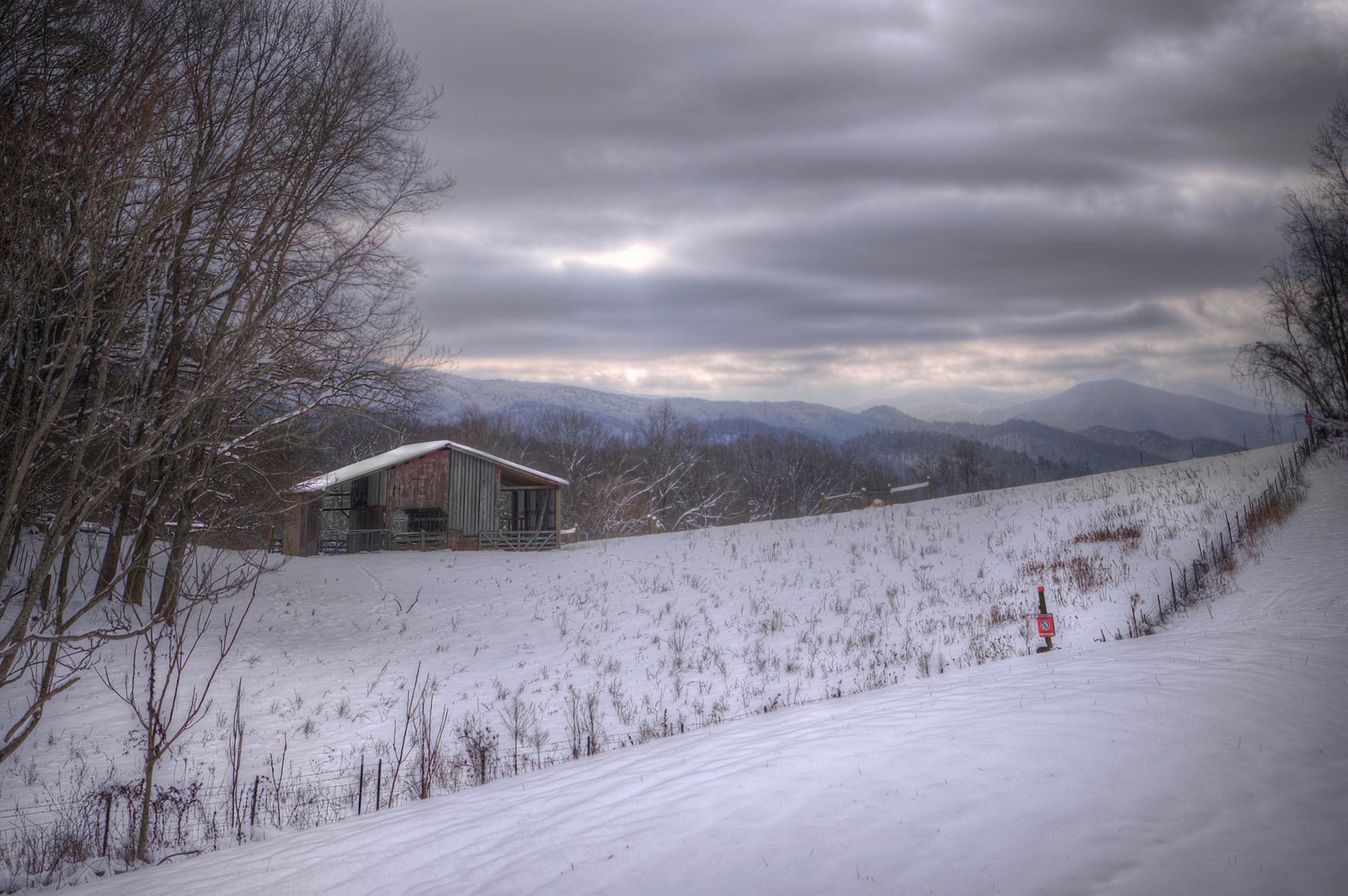 Lone barn on a snow-covered hillside with blue Appalachian ridges receding into the overcast sky