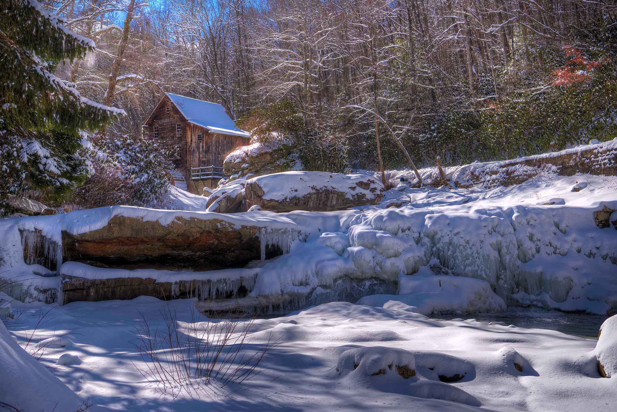 Rustic cabin nestled in a snow-covered forest with a frozen stream and long winter shadows