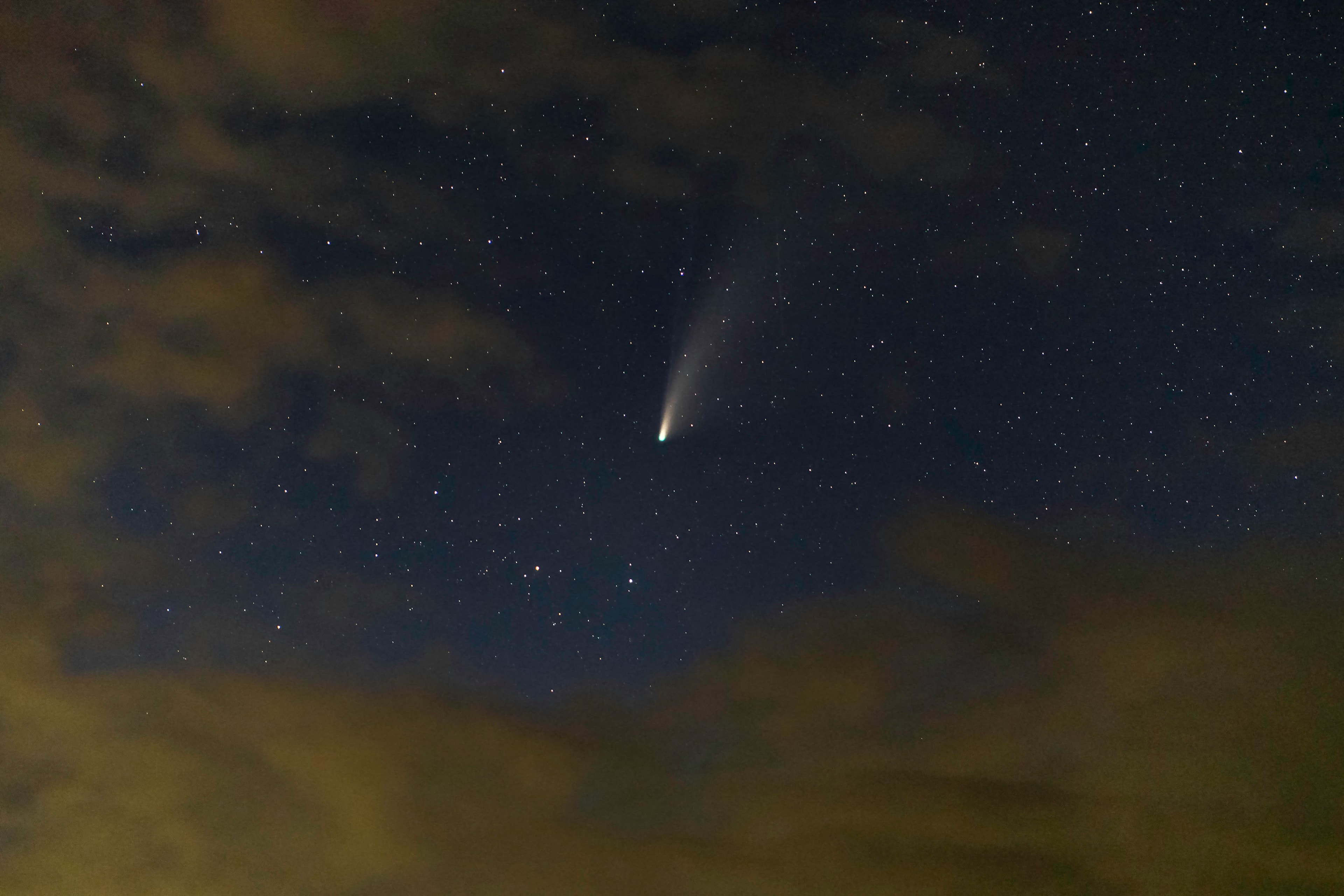 Comet streaking through a deep blue night sky above scattered clouds