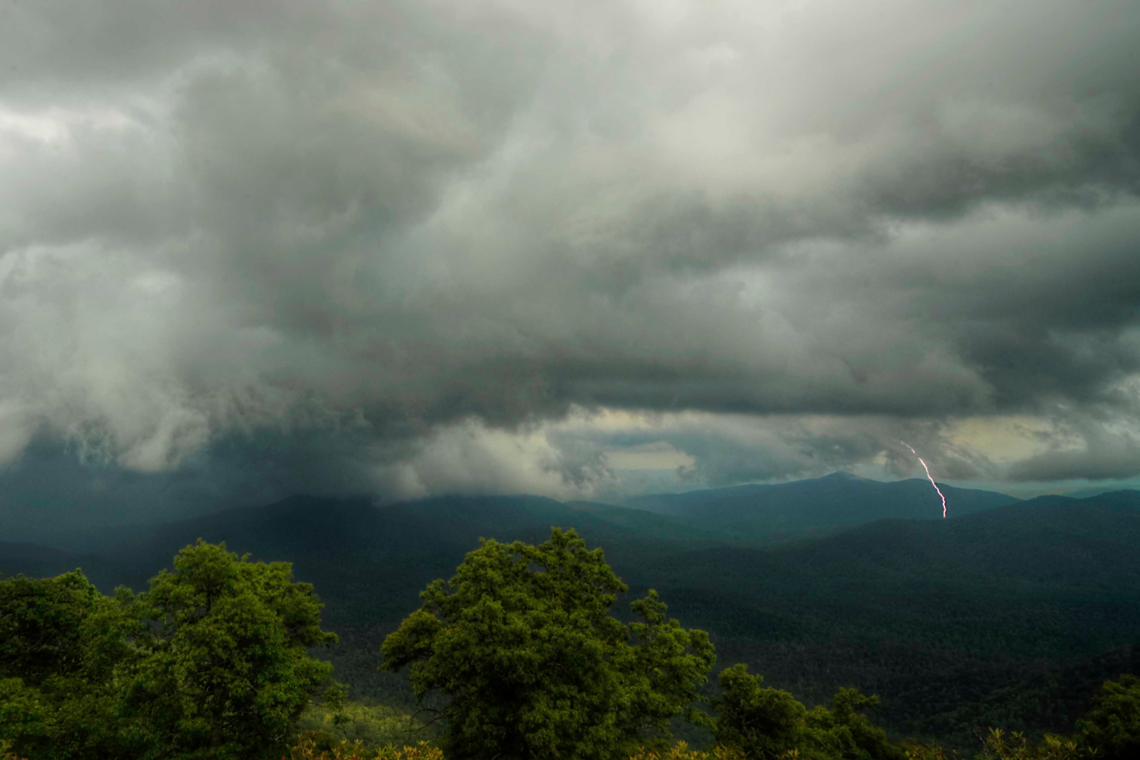 A stormy afternoon in the Blue Ridge Mountains with a lightning bolt striking a distant ridge beneath a roiling dark sky