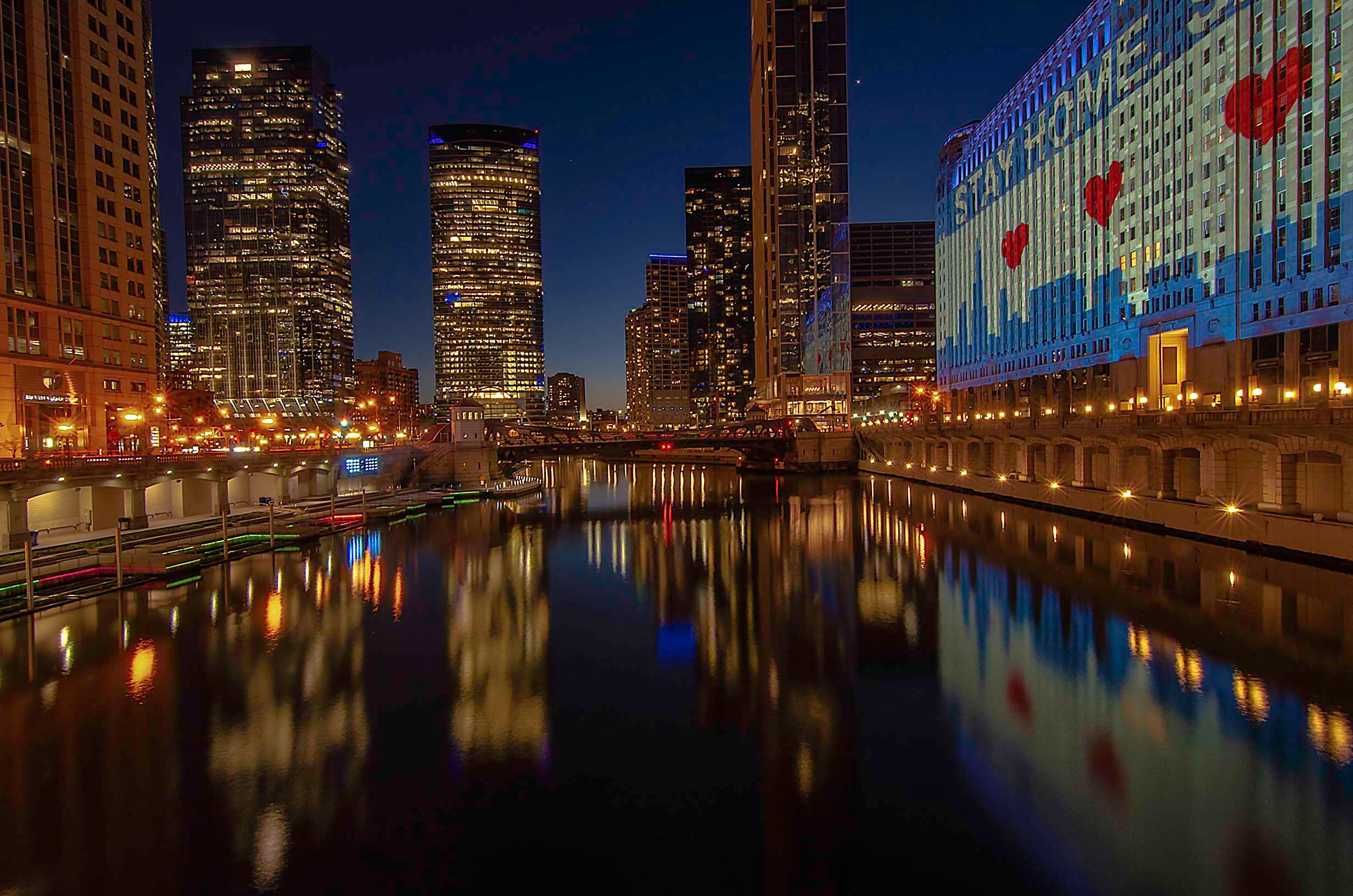 Chicago River at night with skyscrapers and Stay Home projection