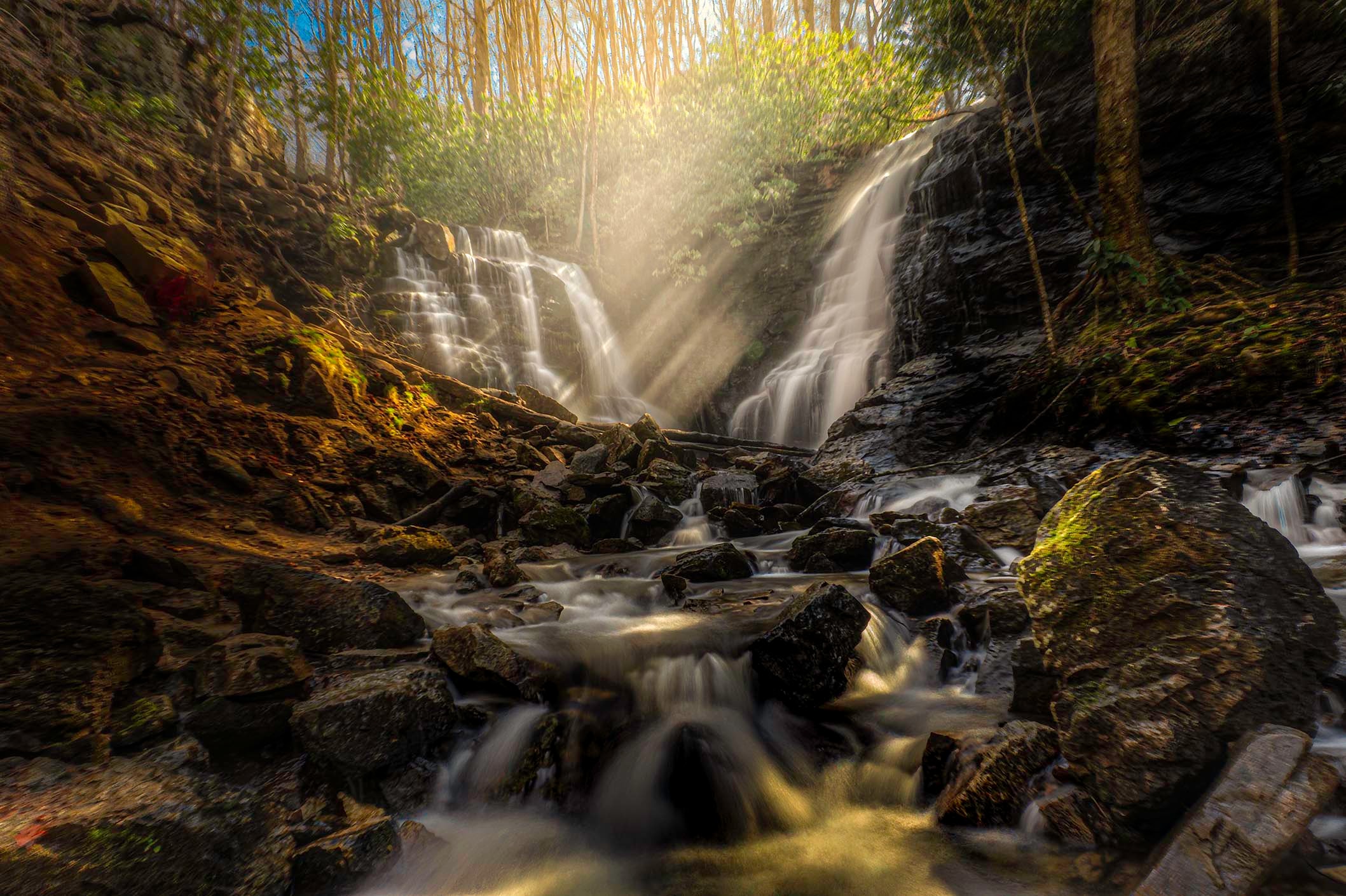 Twin Soco Falls with golden sunbeams streaming through the forest canopy above the cascade